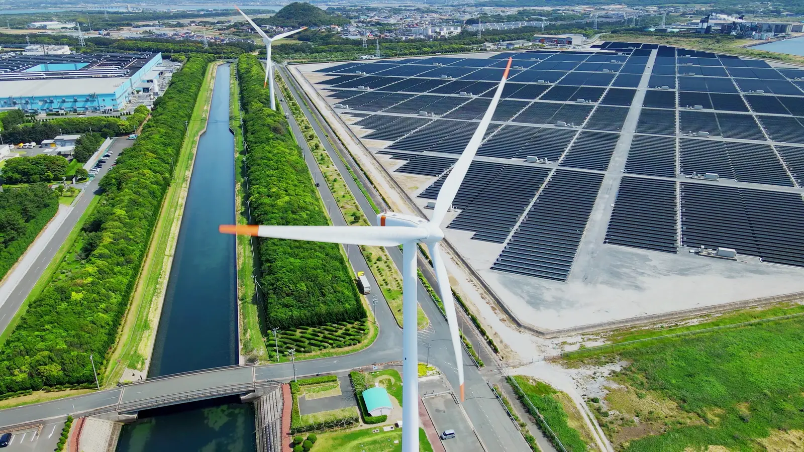 Luftaufnahme eines großflächigen Solarparks mit Windrad entlang eines Kanals